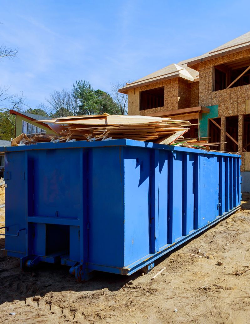 Blue dumpster at construction site with lumber and building materials